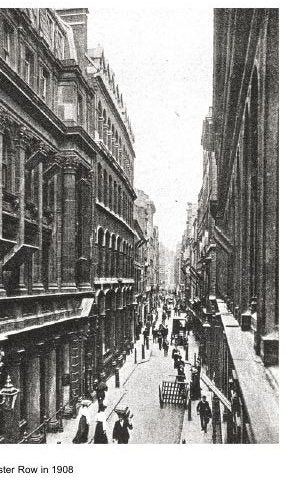 A steep view down a very narrow street between tall commercial buildings, with awnings, hanging shop signs and pedestrians in Edwardian dress.